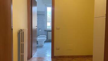 Een smalle gang met een deur die leidt naar een badkamer met toilet en radiator.