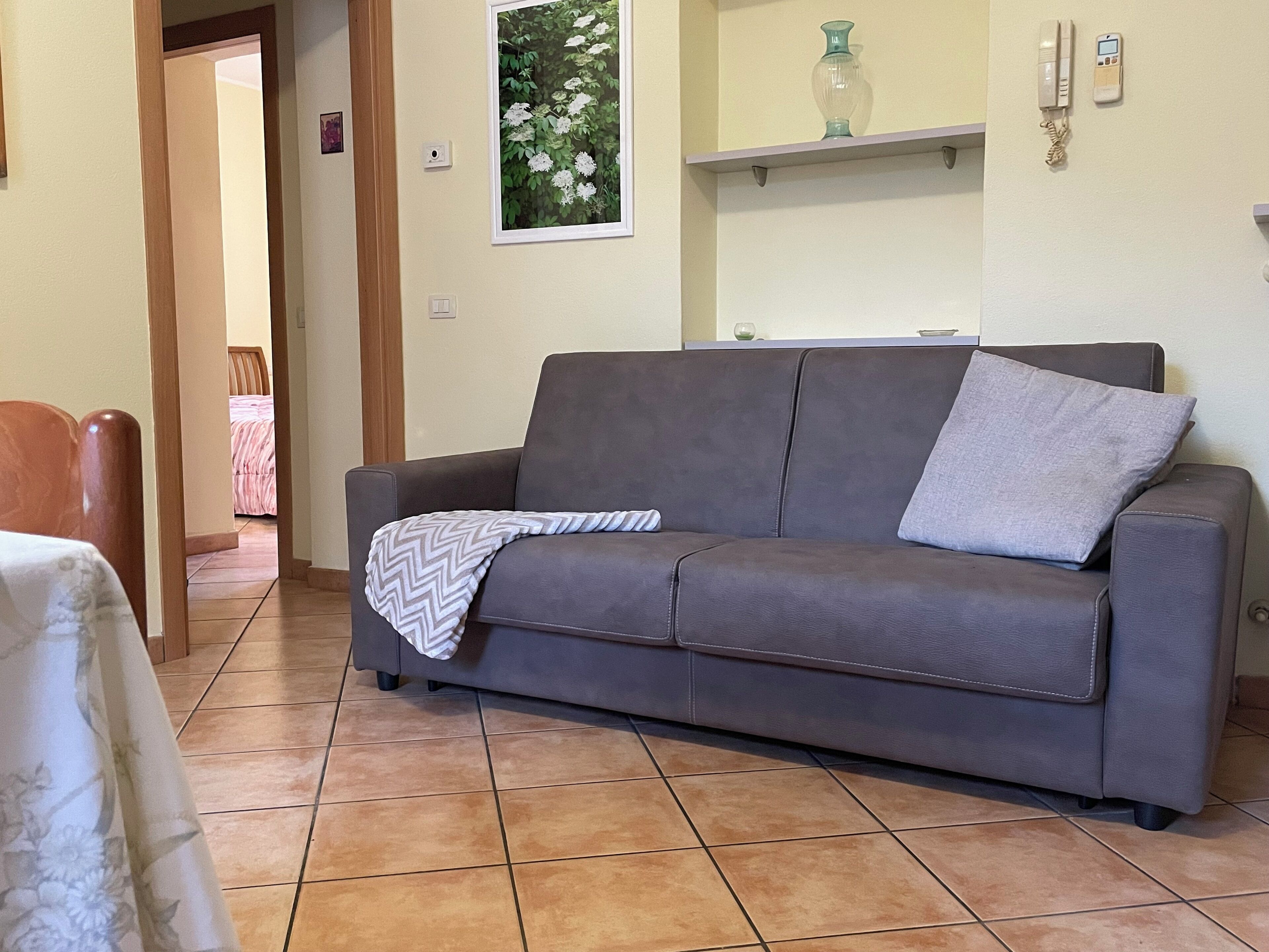 A living room with a grey sofa, a patterned throw blanket, a vase, and a wall-mounted phone.
