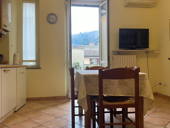 A kitchen with a dining area, a clock, a TV, and a view of a building and trees through a window.