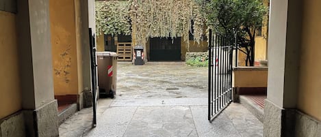 Un patio con suelo de piedra, una puerta y un bote de basura.