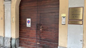 Een bruine houten deur met een 'verboden toegang'-bordje, een plaquette voor 'Studio Legale Associato Madama & Cie' en een andere plaquette voor 'Avvocato Manica Ghigini'.