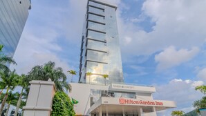 A Hilton Garden Inn building with a modern glass facade, located in a cityscape with palm trees and other buildings. - Modern and Complete Apartments in Itajai - RVC (Itajai)