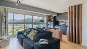 A modern living room with a black sofa, a dining area, and a kitchen with dark cabinets. - Modern and Complete Apartments in Itajai - RVC (Itajai)