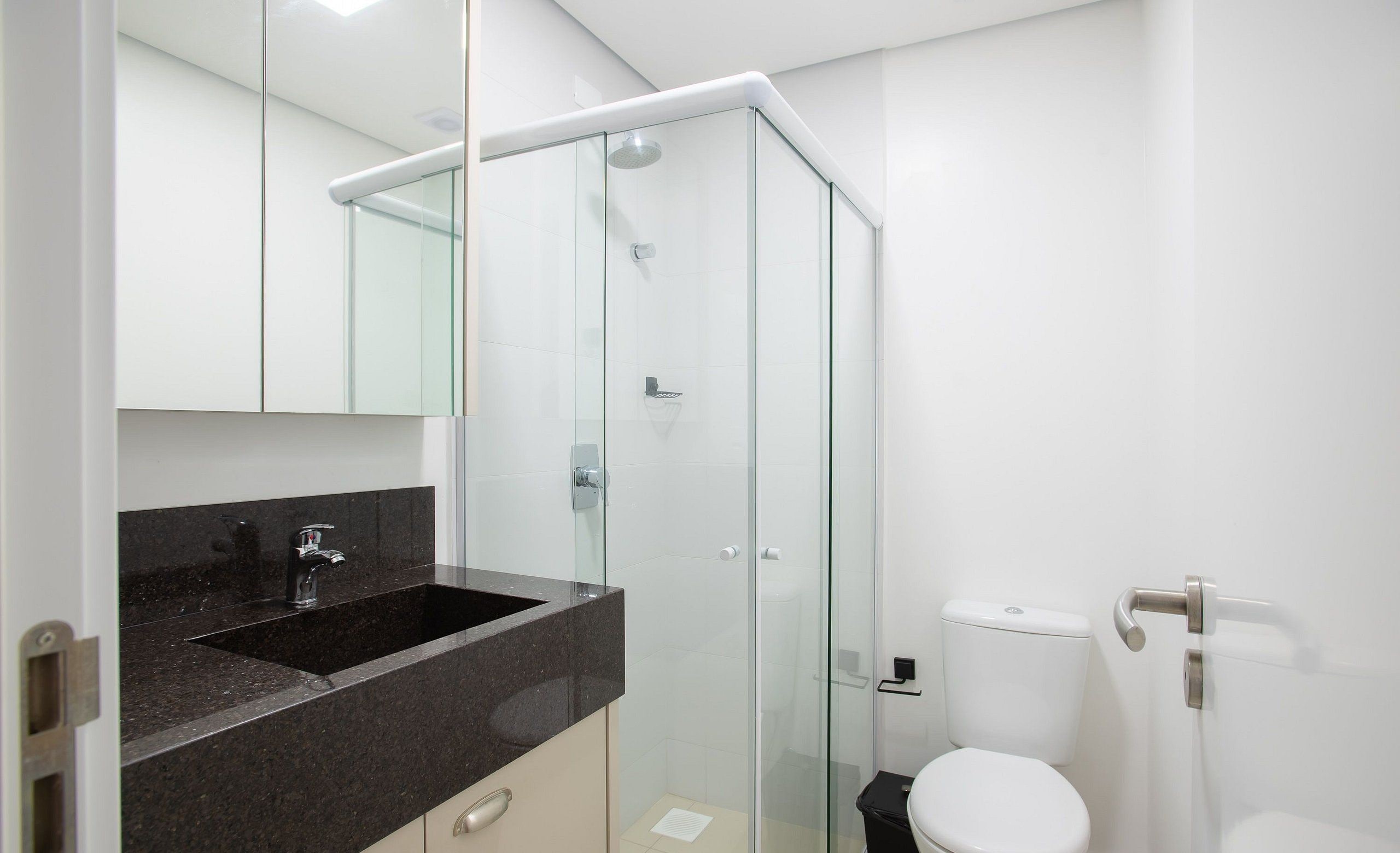 A modern bathroom with a glass shower enclosure, a sink with a dark countertop, and a toilet.