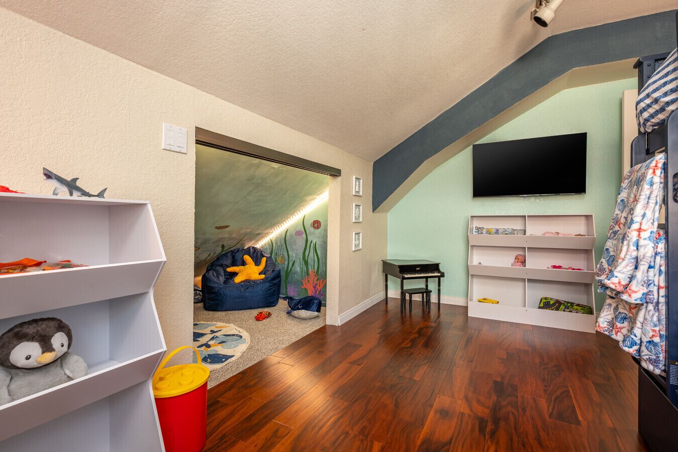 A child's playroom with a wooden floor, a bean bag, a piano, and a TV.