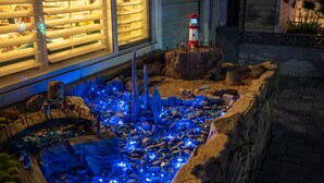 Modelo de un paisaje costero con un faro, terreno rocoso y un pequeño estanque iluminado con luces azules.
