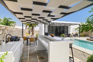 En modern uteplats med pool, grill och en sittgrupp med utsikt över poolen.