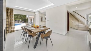 A modern dining area with a wooden table and chairs, a view of a swimming pool, and a staircase leading to an upper level. - Villa Caripira by Villa Plus (Albufeira)