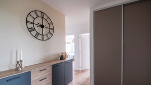 Een moderne kamer met een houten vloer, een blauwe kast met lades, een grote wandklok en een schuifdeurkast.