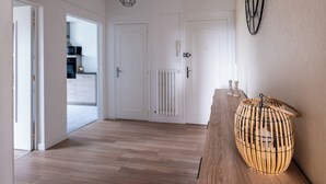 Een gang met houten vloer, witte deuren en een rieten mandje op een houten tafel.