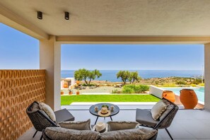 Un balcón con vista al mar, una piscina y mobiliario de exterior.