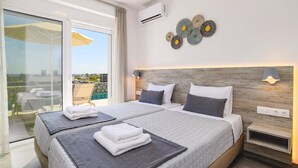Een moderne hotelkamer met een groot bed, twee nachtkastjes, een wandairconditioner, decoratieve wandkunst en uitzicht op het omliggende landschap.