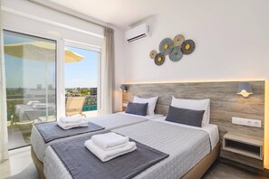 Ein modernes Hotelzimmer mit einem großen Bett, zwei Nachttischen, einer Wand-Klimaanlage, Wanddekoration und Blick ins Freie.