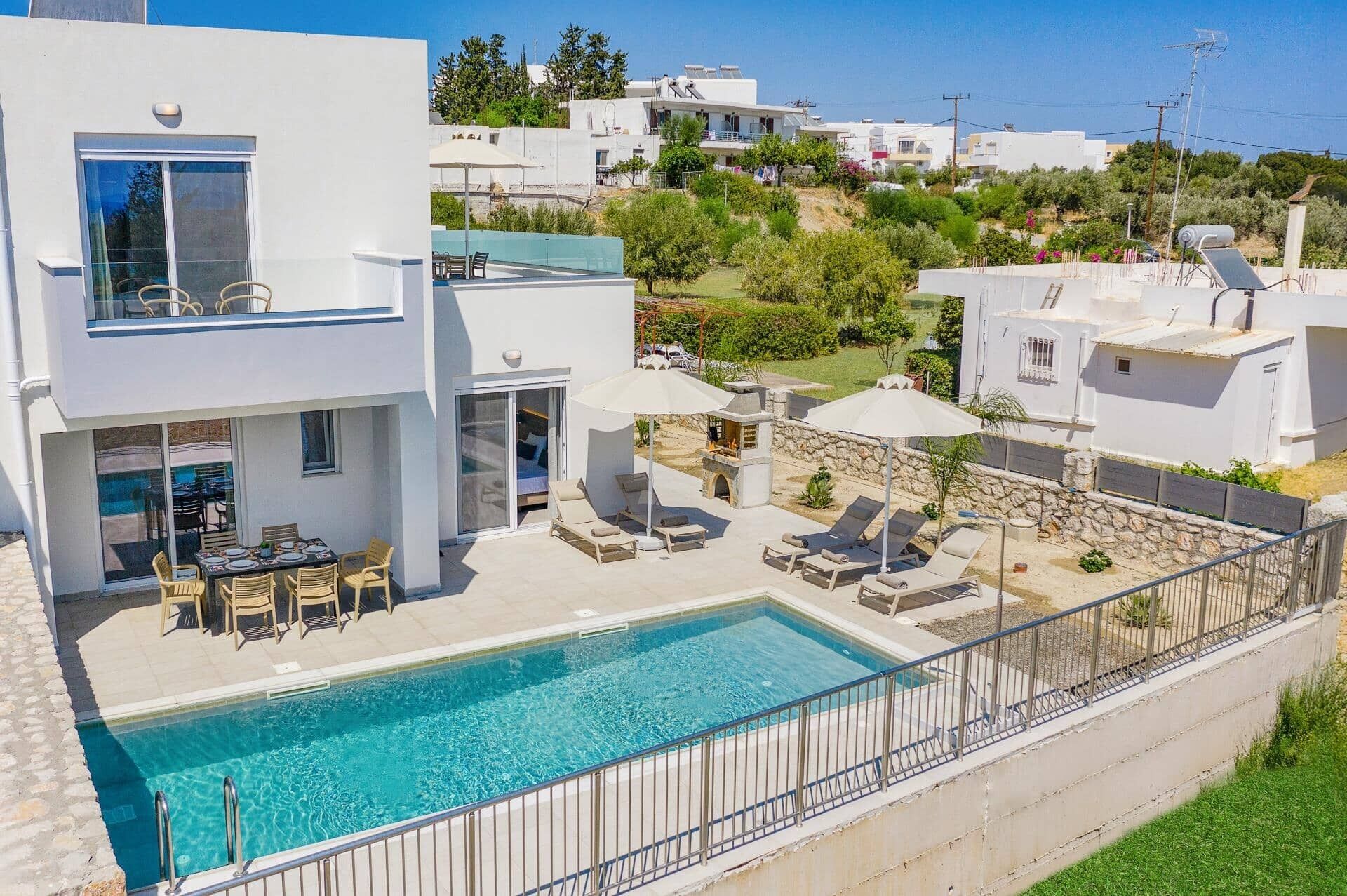 A modern villa with a swimming pool, outdoor seating, and a view of the surrounding hillside.