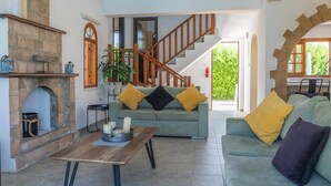 Ein geräumiges Wohnzimmer mit Kamin aus Stein, einer Holztreppe und einem grünen Sofa mit gelben Kissen.
