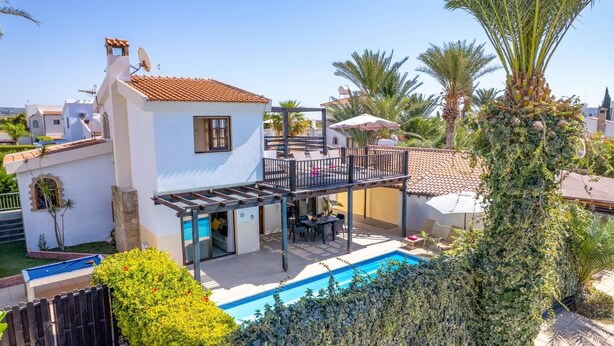Ein zweistöckiges Haus mit Balkon, Pool und umgebender Bepflanzung.
