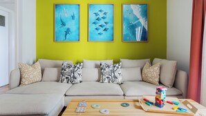 Una sala de estar con un sofá, cojines, una mesa de centro con bloques y tres obras de arte enmarcadas en la pared.