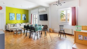 Un espacio moderno con zona de comedor, sofá, televisor y ventana con cortinas.