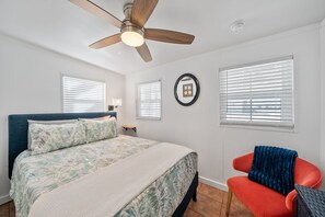 Un dormitorio con una cama, un ventilador de techo y dos ventanas con persianas.