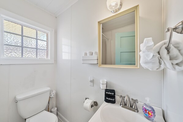 A bathroom with a toilet, sink, and mirror. - Key Lime Cottage - 1930's 2 Bed 2 Bath Beach Cottage - Steps From The Sand! (Panama City Beach)