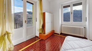 Habitación de hotel con cama, armario, radiador y ventana con vistas a la montaña.