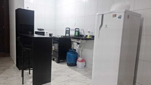 A kitchen with a refrigerator, a microwave, a sink, a gas cylinder, and a trash bin. - Apartamento novo em João Pessoa  (João Pessoa)