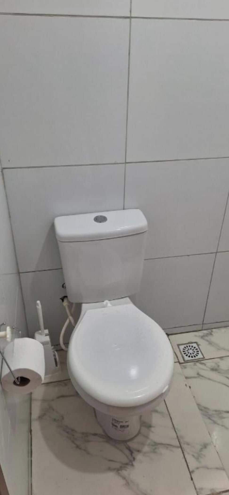 A toilet with a marble floor, a toilet paper holder, and a flush handle.