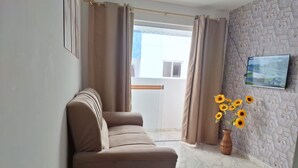 A living room with a sofa, a wall-mounted TV, a vase with sunflowers, and a patterned wall. - Apartamento novo em João Pessoa  (João Pessoa)