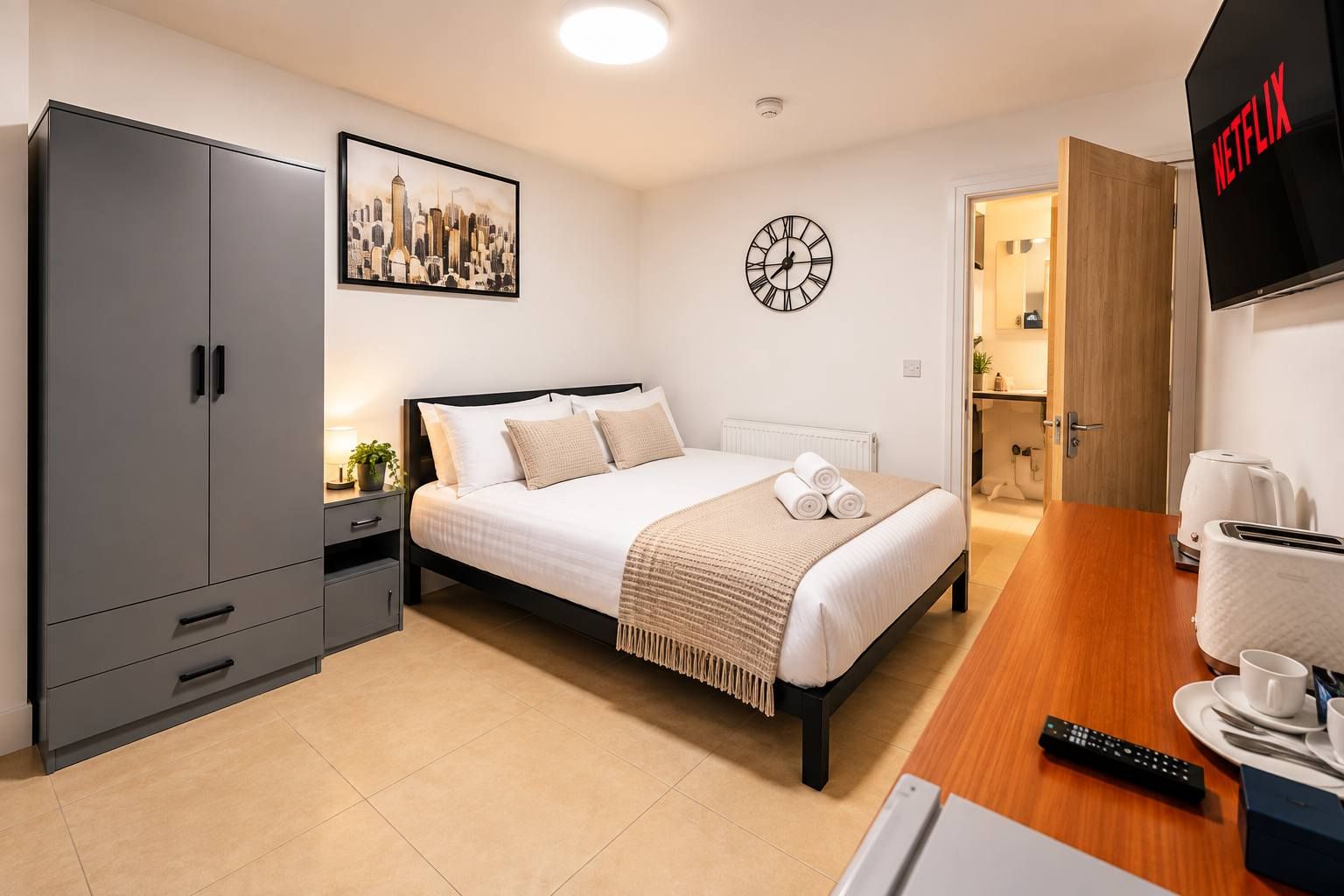 A modern hotel room with a bed, wardrobe, bedside table, clock, and a TV displaying the Netflix logo.