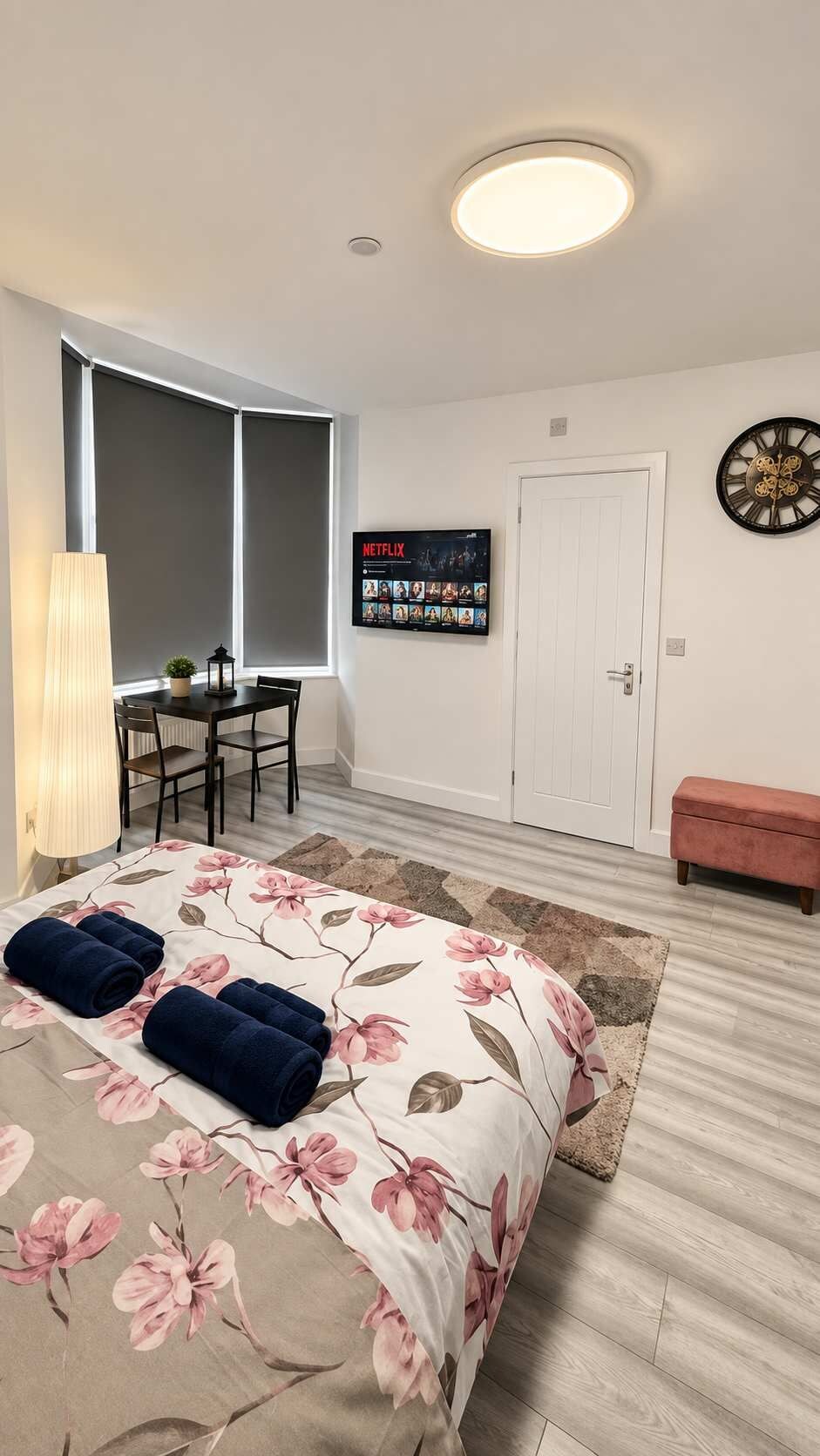 A bedroom with a bed, a desk, a TV, a clock, and a door.