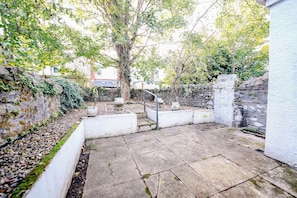 A stone-paved courtyard with a tree, stone walls, and a white building in the background. - Boutique Roath Studio (Cardiff)