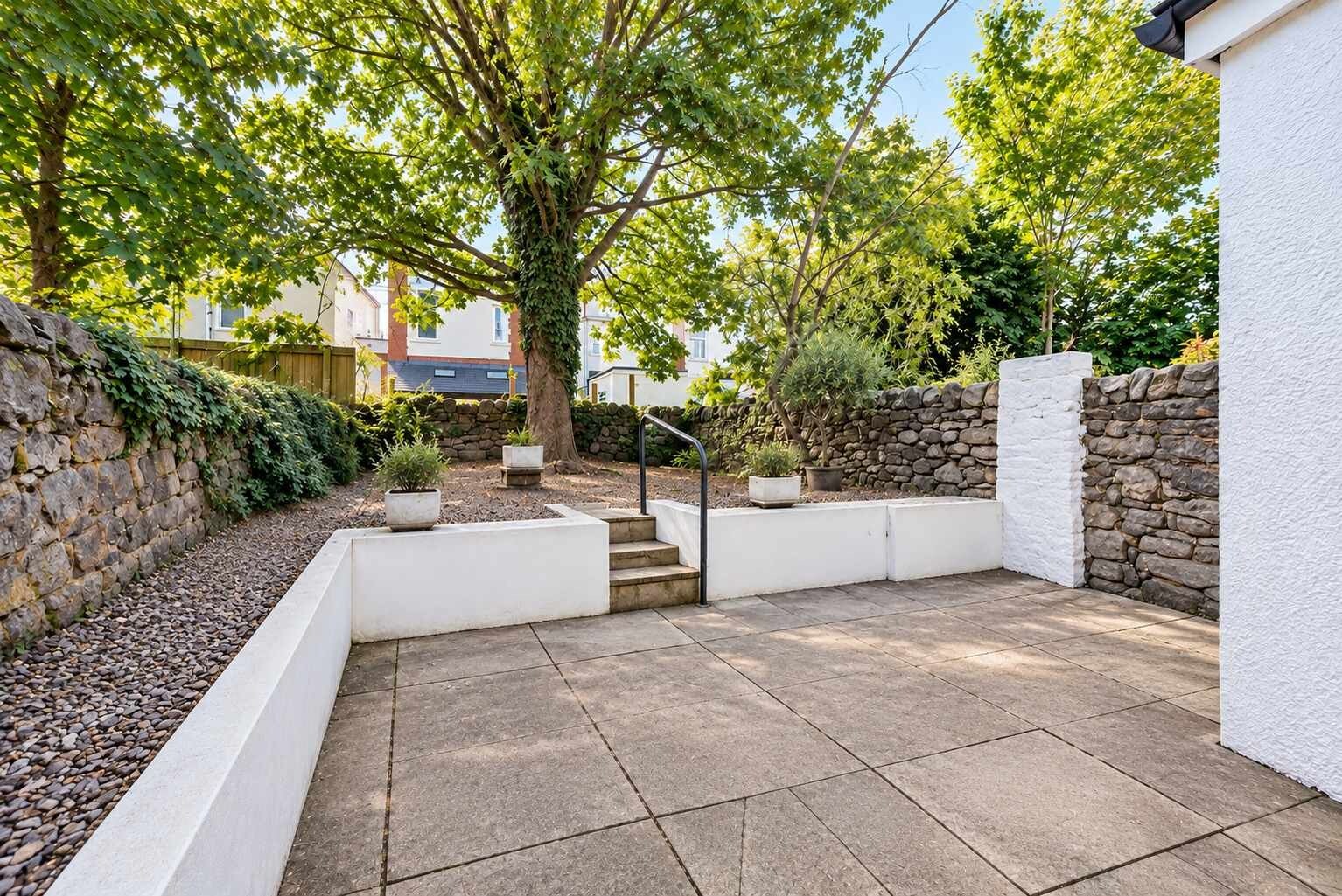 A patio area with stone walls, potted plants, and a staircase leading to an upper level.