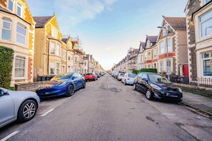 Eine Straße gesäumt von Reihenhäusern, parkenden Autos und einem klaren Himmel.