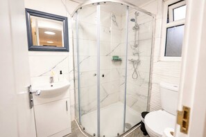 Ein modernes Badezimmer mit einer gläsernen Duschkabine, einem Waschbecken mit Pflegeprodukten und einer Toilette.