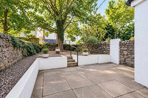 A patio area with stone walls, potted plants, and a staircase leading to an upper level. - Cozy Modern Studio: (Cardiff)