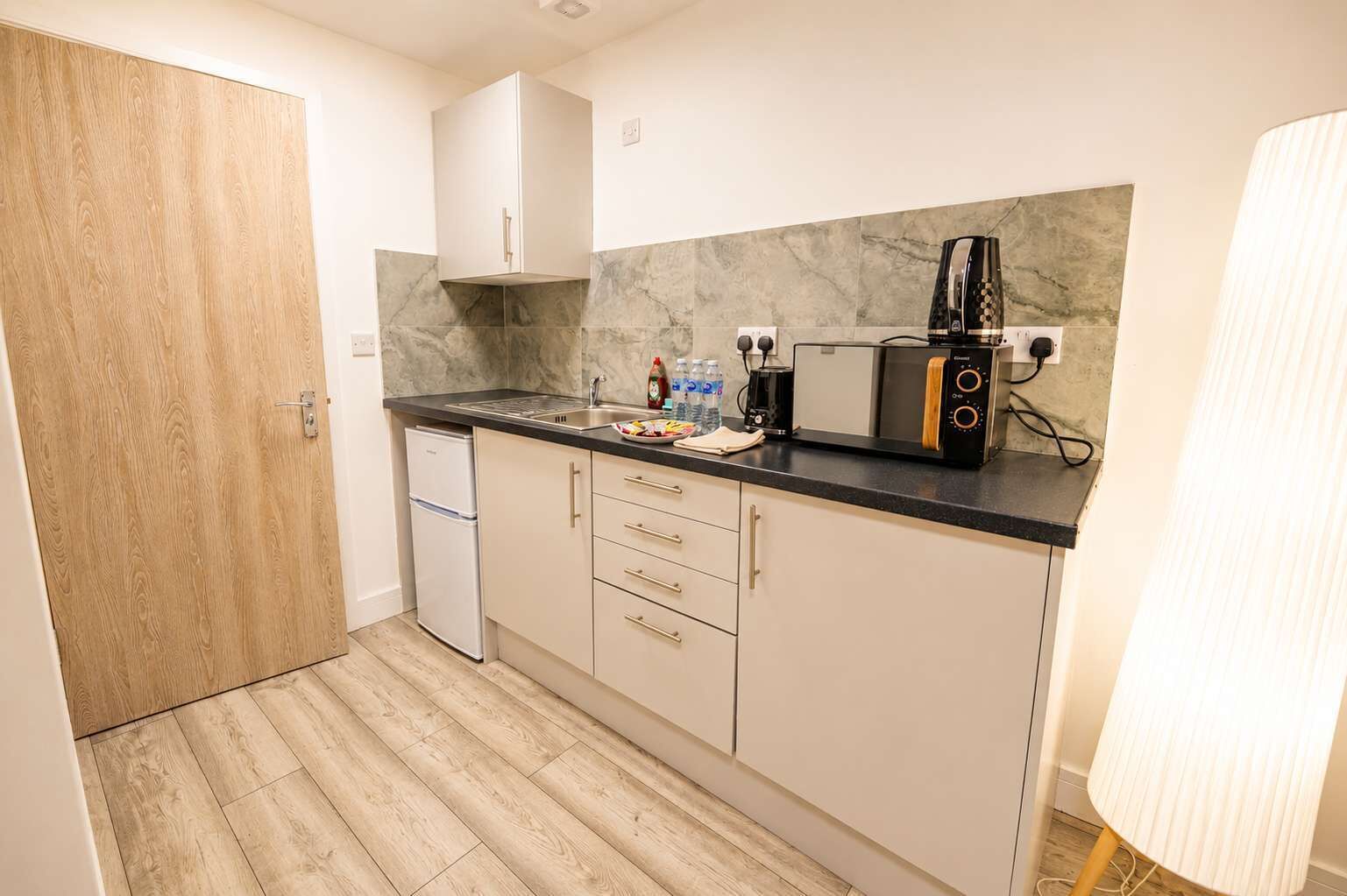 A compact kitchen with a refrigerator, microwave, toaster, and a sink.