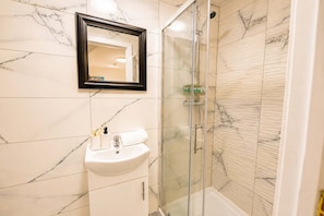 A bathroom with a marble sink, a glass-enclosed shower, and a mirror above the sink. - Cardiff Studio Getaway: Hot Tub • WIFI (Cardiff)
