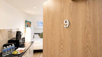 A modern kitchen with a wooden door marked with the number 9, a coffee maker, and a breakfast bar with water bottles and a fruit plate.