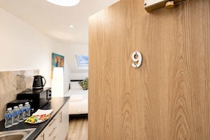Een moderne keuken met een houten deur met het nummer 9, een koffiezetapparaat en een ontbijtbar met waterflessen en een schaal fruit.