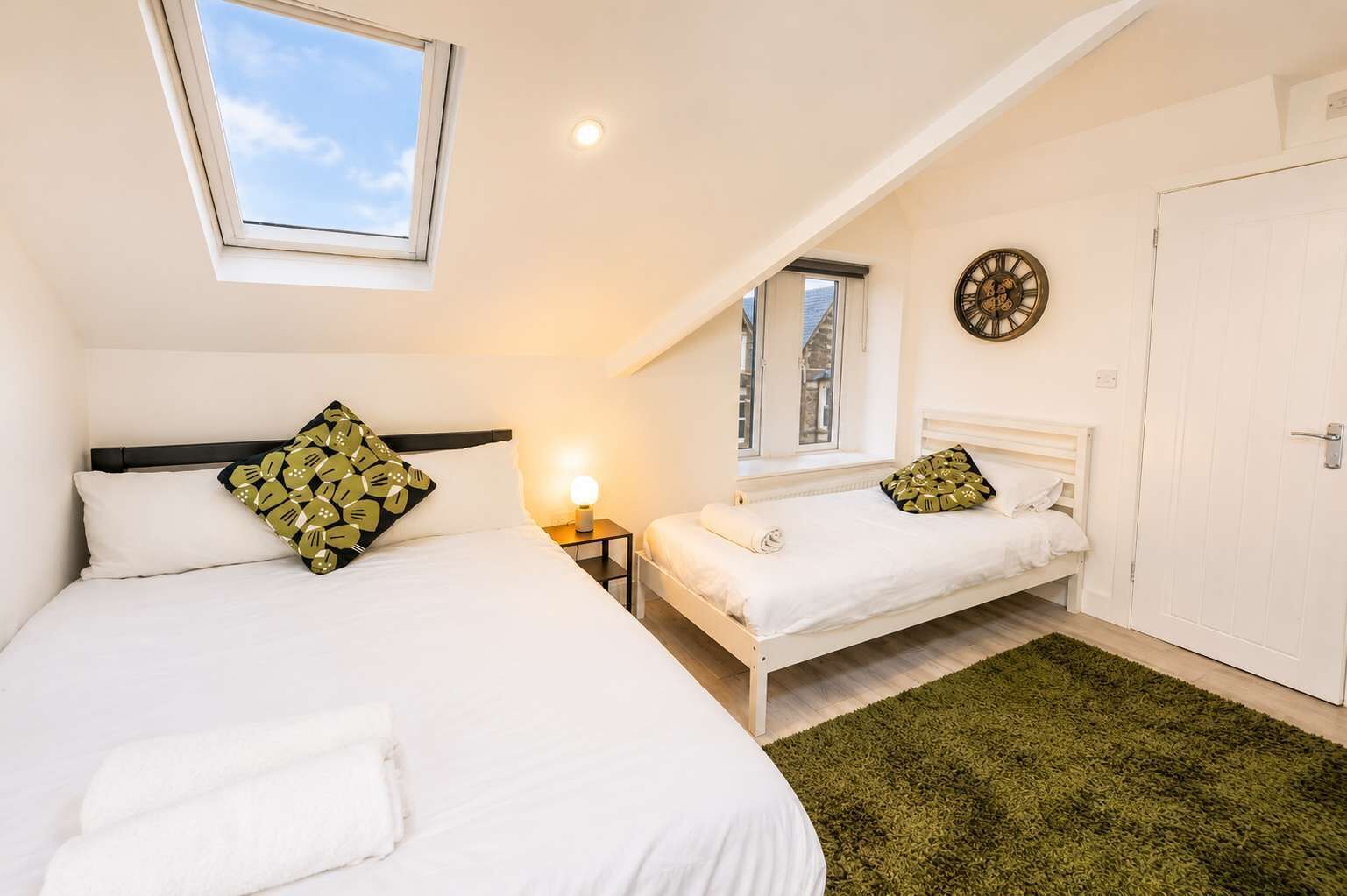 A bedroom with two beds, a skylight, a wall clock, and a door.