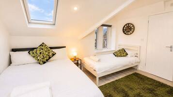 A bedroom with two beds, a skylight, a wall clock, and a door.