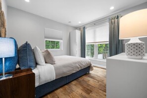 A bedroom with a bed, a nightstand, a lamp, a window with curtains, and a view of greenery outside. - Walk Downtown | Private Patio | Pool | Pets | Skye (Dunedin)