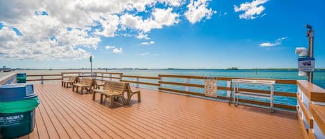 Une terrasse en bois, dotée de bancs et d’une poubelle, qui offre une vue sur une étendue d’eau sous un ciel dégagé.