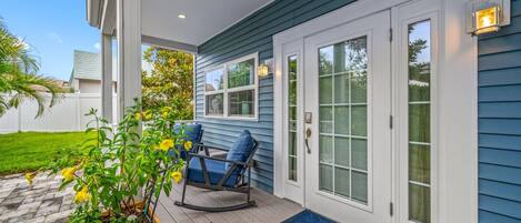A covered porch with a wooden bench, a potted plant, and a door with a glass panel.