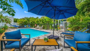 A poolside area with a blue umbrella, lounge chairs, and a small table with a plant.
