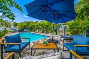 A poolside area with a blue umbrella, lounge chairs, and a small table with a plant. - Walk Downtown | Private Patio | Pool | Pets | Skye (Dunedin)