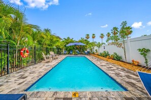 A swimming pool with lounge chairs and umbrellas, surrounded by palm trees and a white fence. - Walk Downtown | Private Patio | Pool | Pets | Skye (Dunedin)