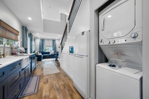 A modern kitchen with a built-in washer and dryer, a wooden floor, and a staircase leading to an upper level. - Walk Downtown | Private Patio | Pool | Pets | Skye (Dunedin)