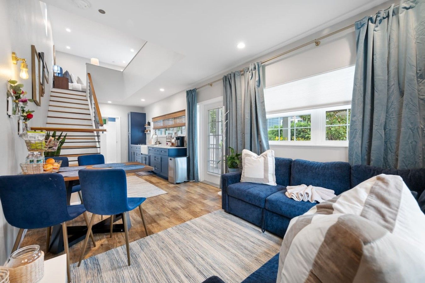 A modern living room with a blue sofa, a dining area with a wooden table, and a kitchen in the background.