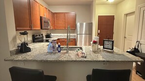 A modern kitchen with granite countertops, wooden cabinets, stainless steel appliances, and a central island with two bar stools.
